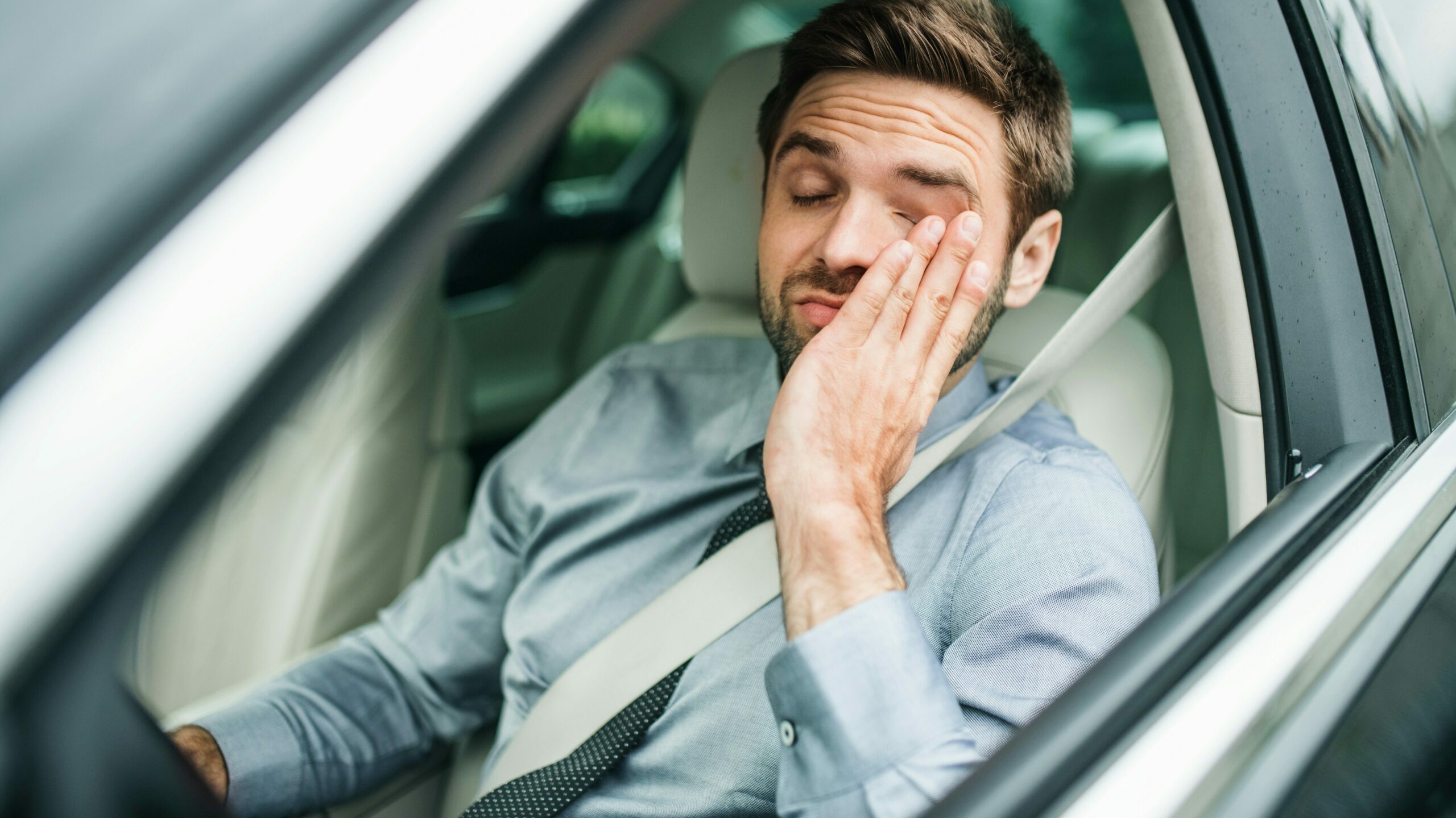 Mann der im Auto am Fahersitz sitz, sichtlich müde und erschöpft sein Gesicht reibt.